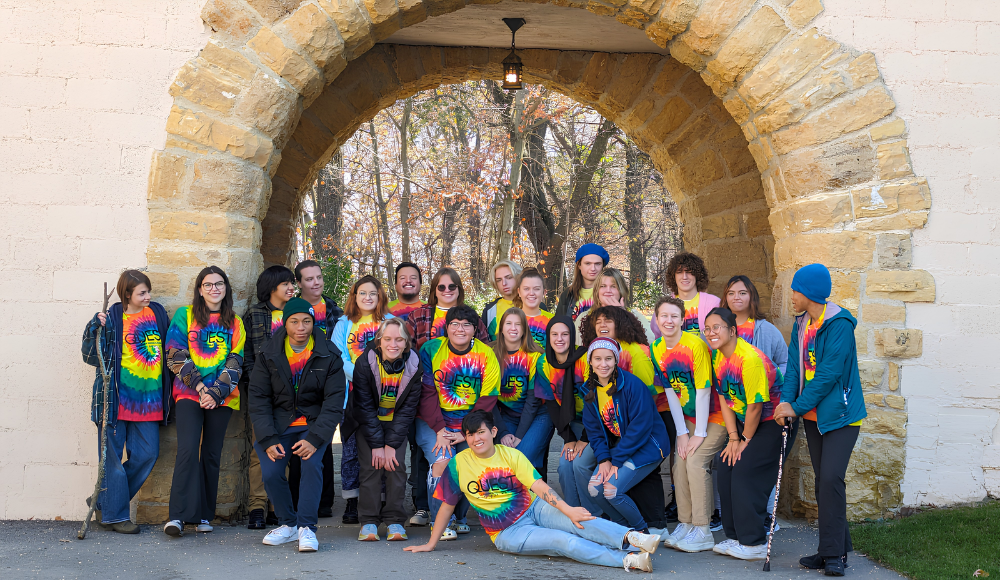 Students in the LGBTQIA+ Initiatives program pose together for a group photo under a stone arch.